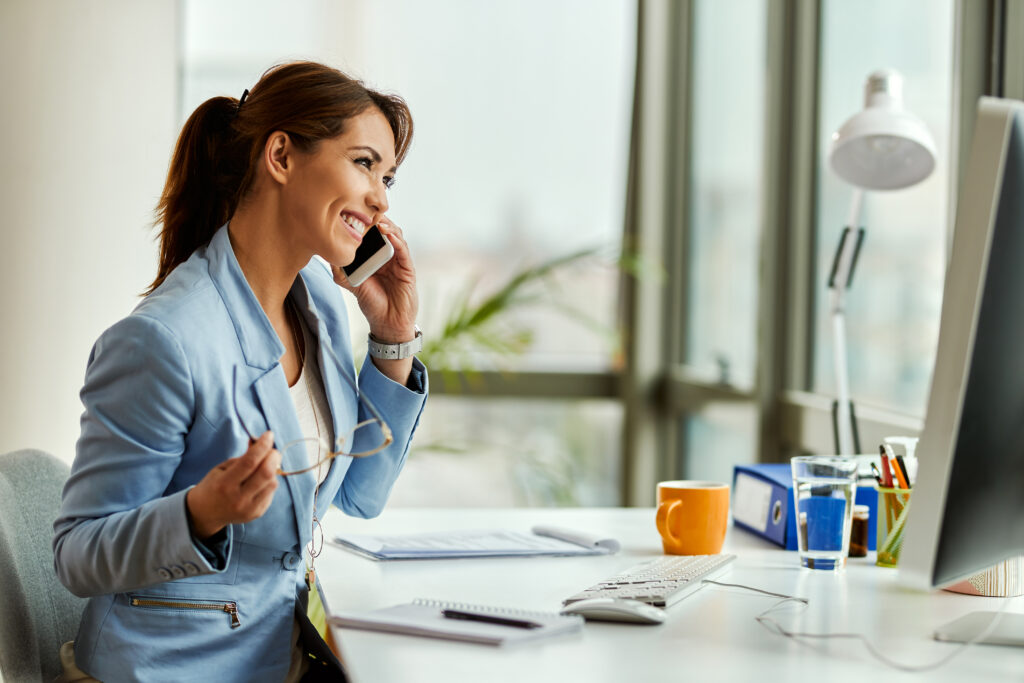 Young happy businesswoman using cell phone and making a phone call in the office.